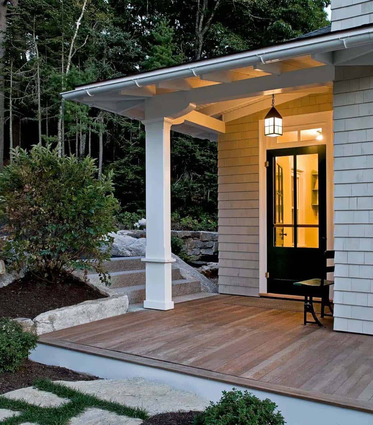 Covered side porch with wood deck and stone steps at twilight