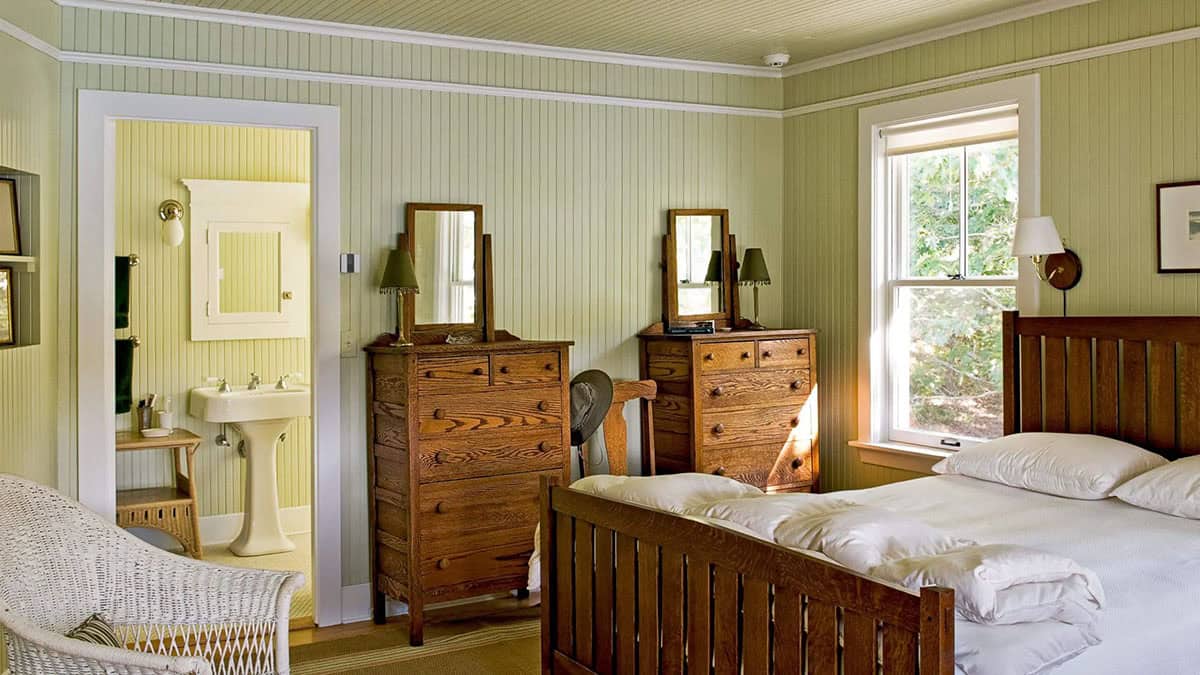 Green-paneled bedroom with antique dressers and wicker chair
