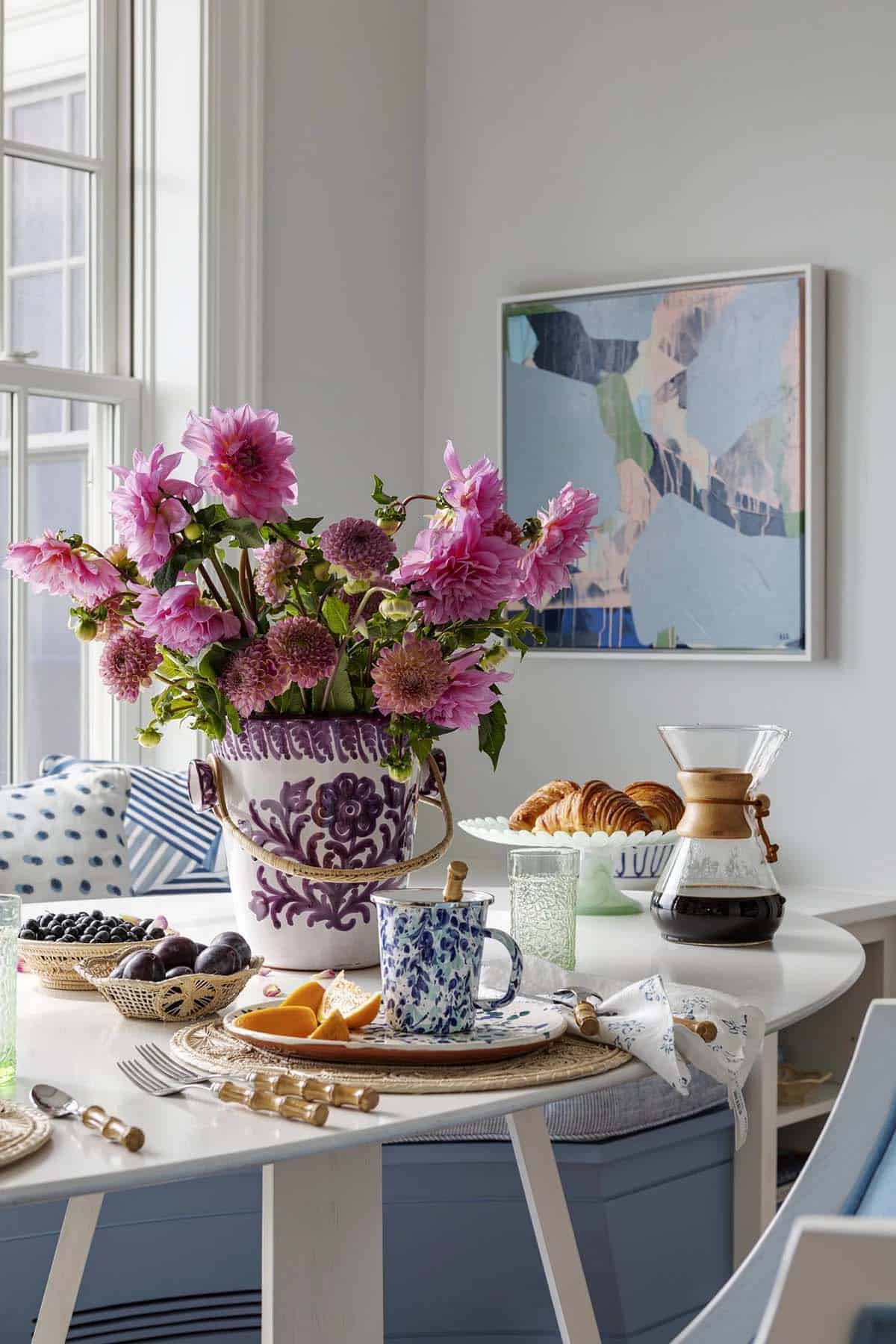 Pink dahlias in patterned vase beside croissants and coffee setup