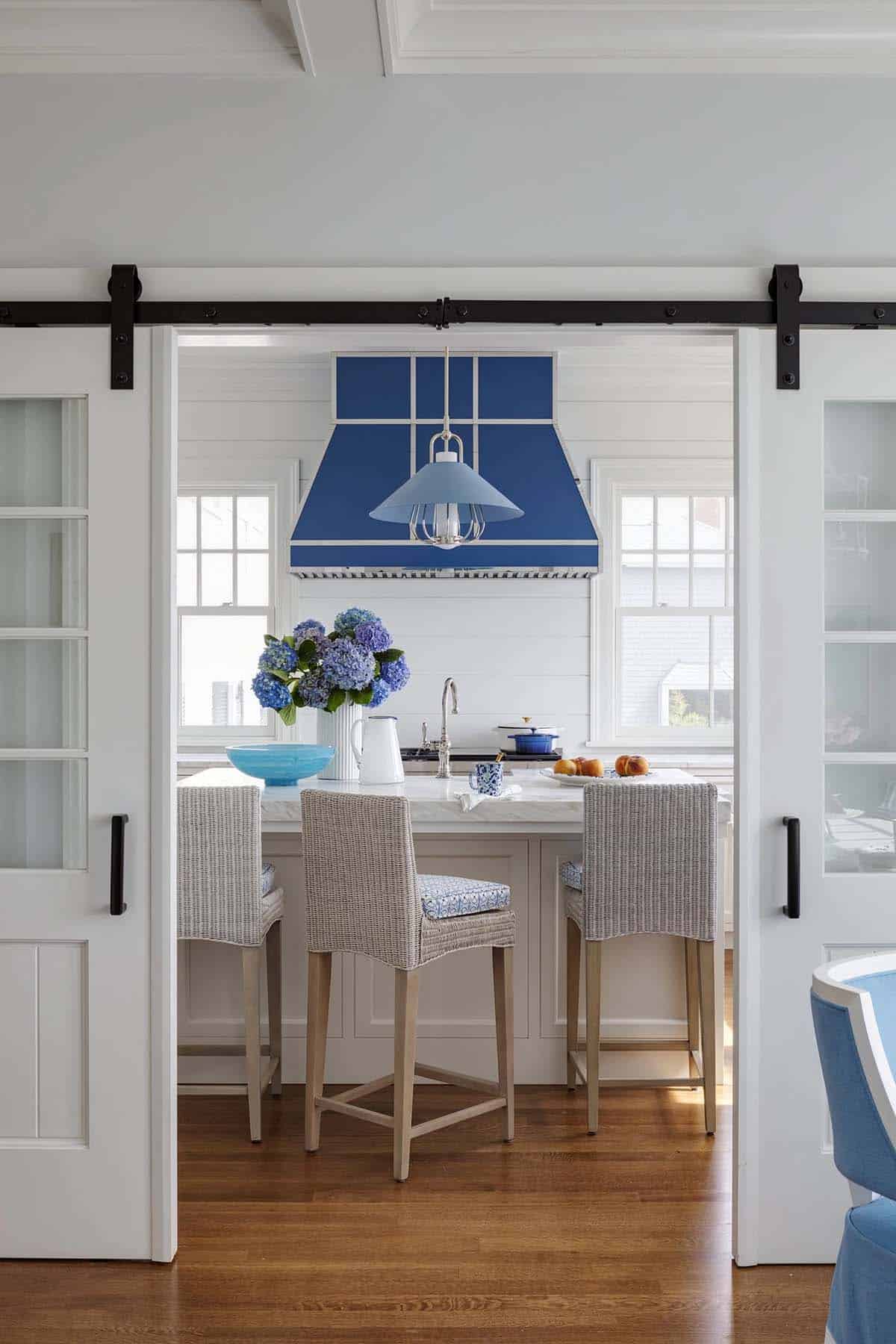 Cobalt blue kitchen hood over marble island with woven barstools