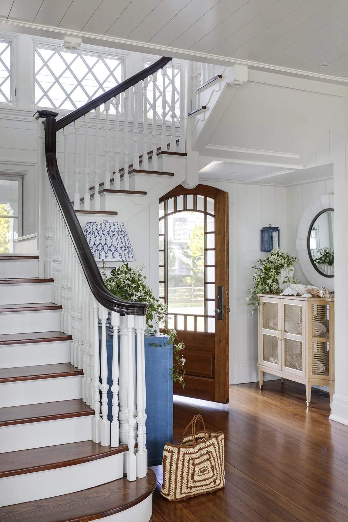 Curved staircase with dark wood railing and arched front door 