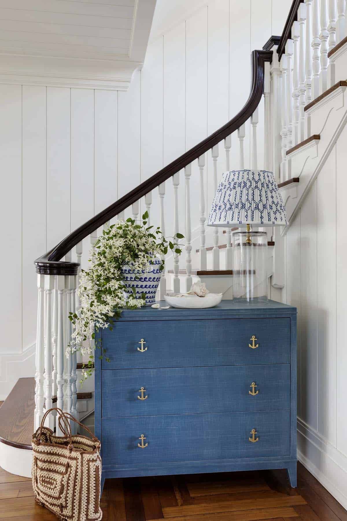Blue anchor-hardware dresser beneath curved staircase with white flowers