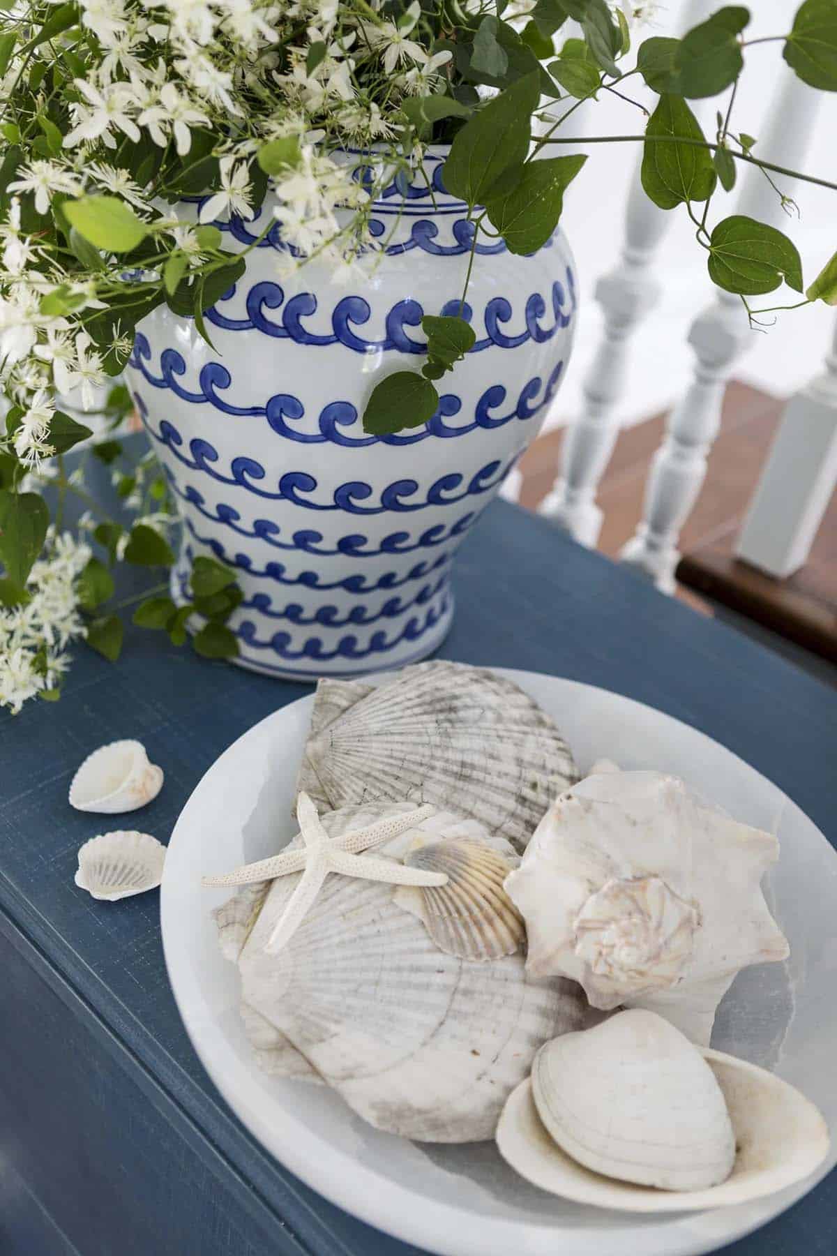 Wave-patterned vase with clematis beside a bowl of seashells