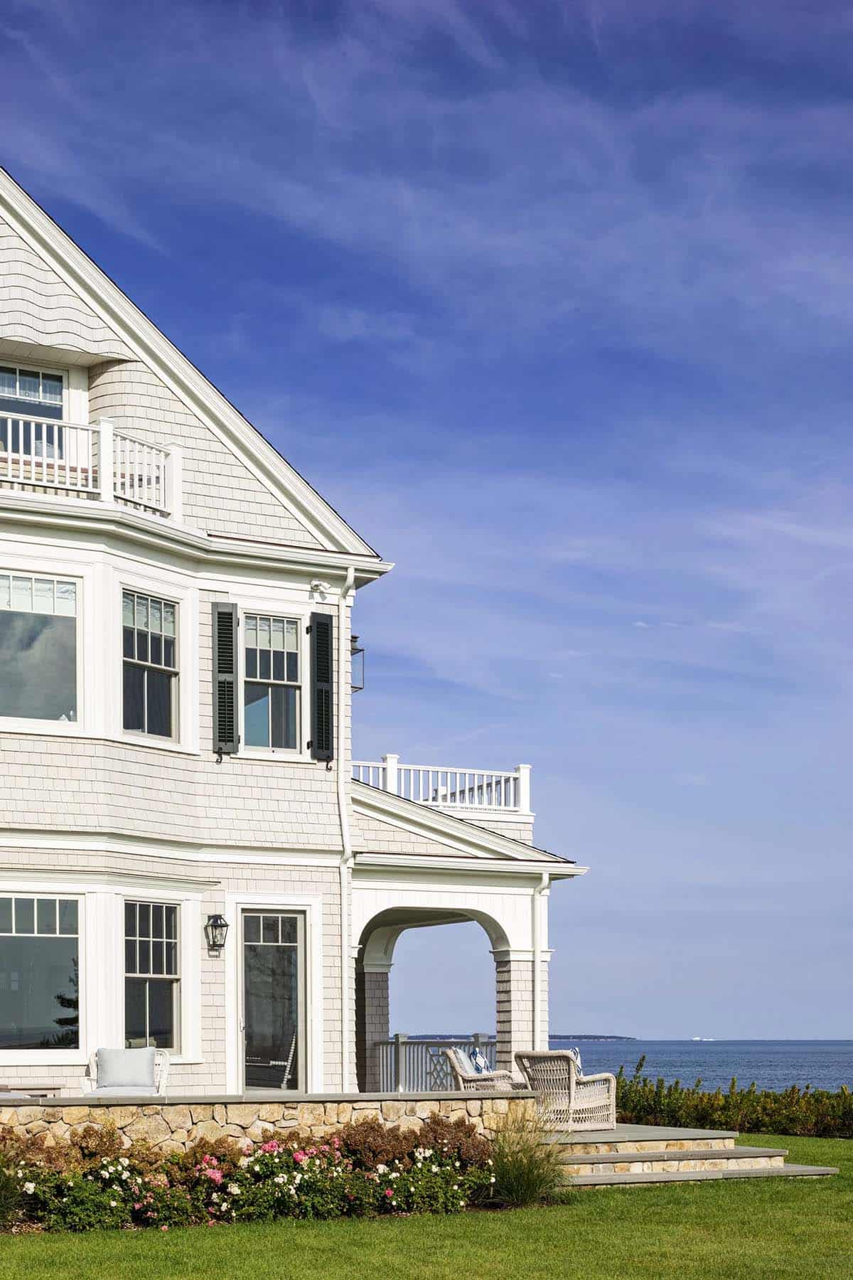 Shingle-style home exterior with black shutters and stone patio