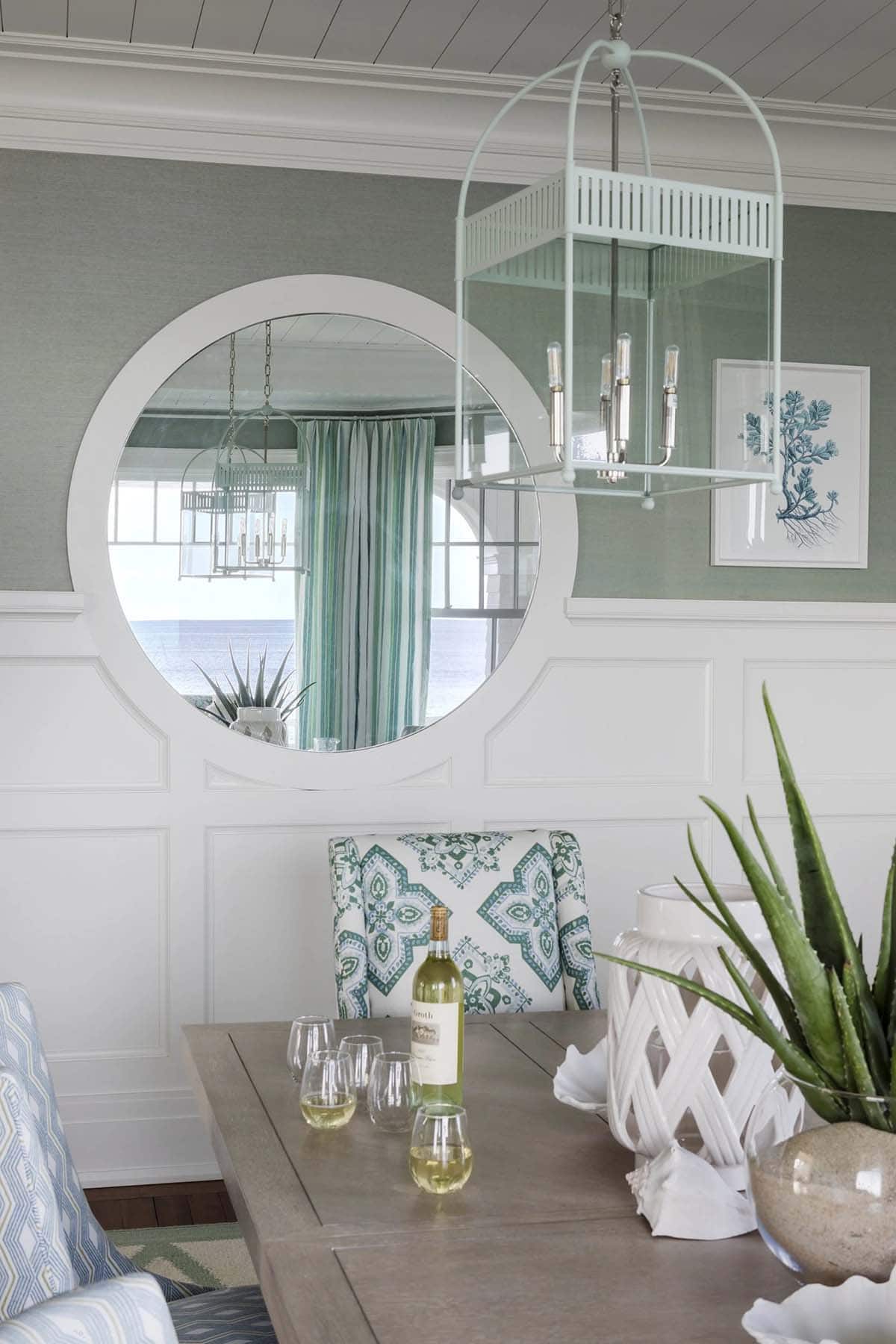 Round mirror reflecting dining room chandelier and ocean beyond