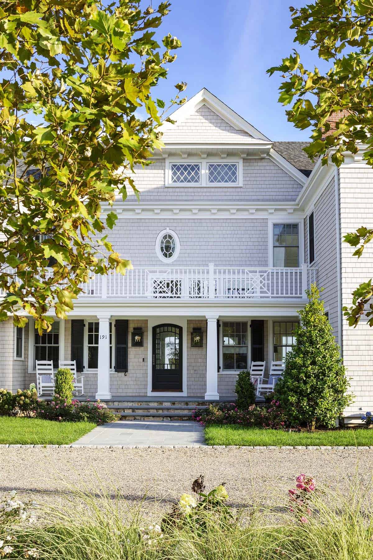 Front porch of shingle-style home with white rocking chairs