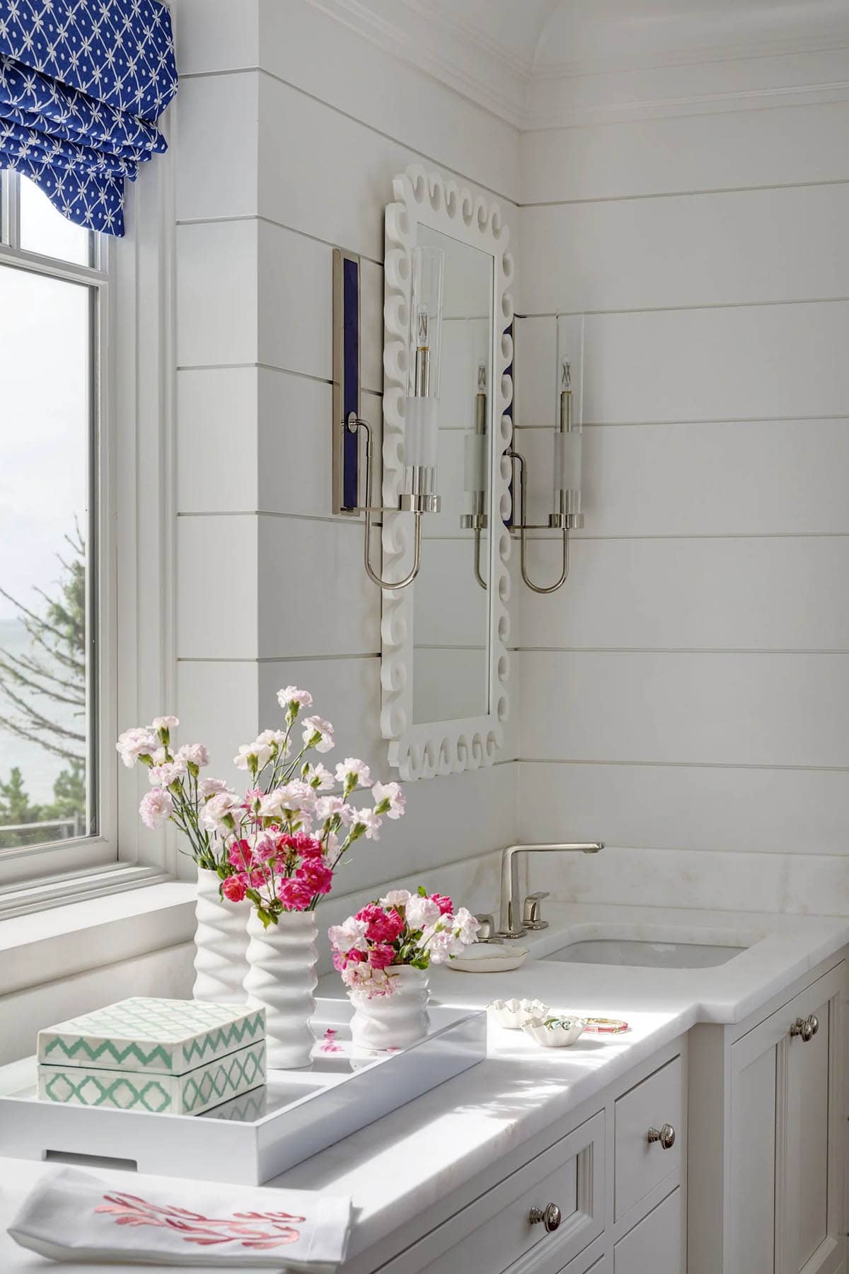 Bathroom counter styled with pink florals and scalloped mirror