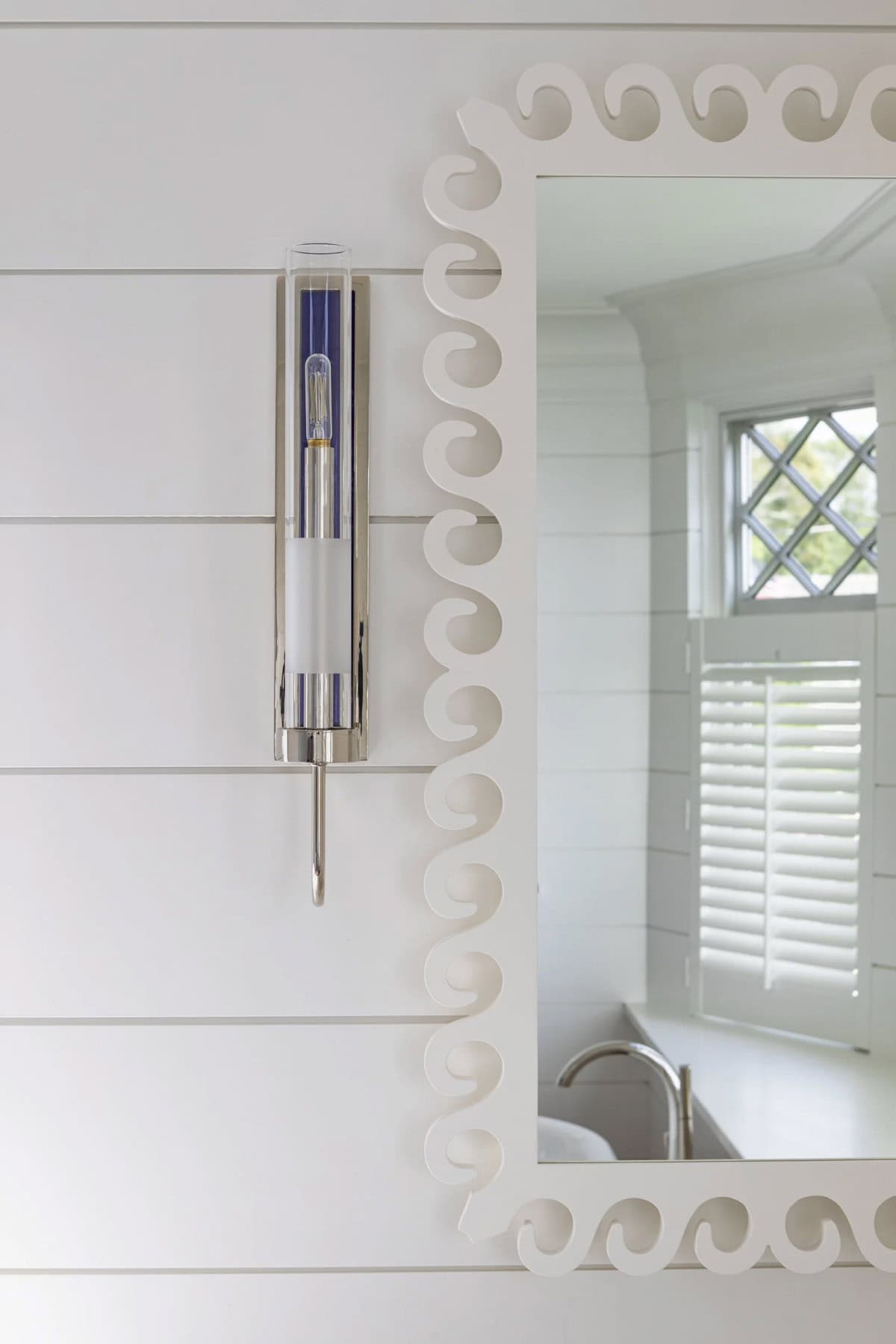 Detail of scalloped white mirror and nickel wall sconce