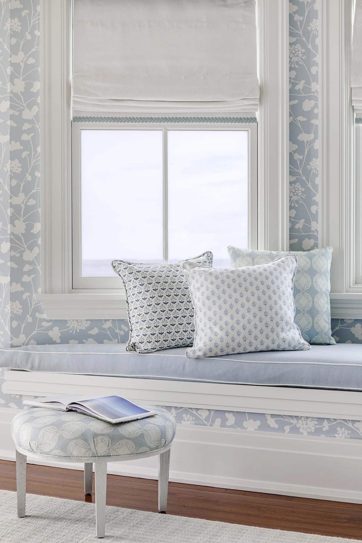 Window seat with patterned throw pillows and round tufted ottoman