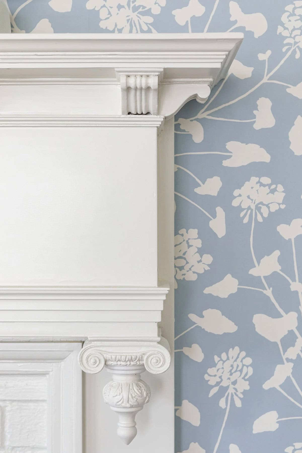 Detail of white fireplace mantel against blue floral wallpaper