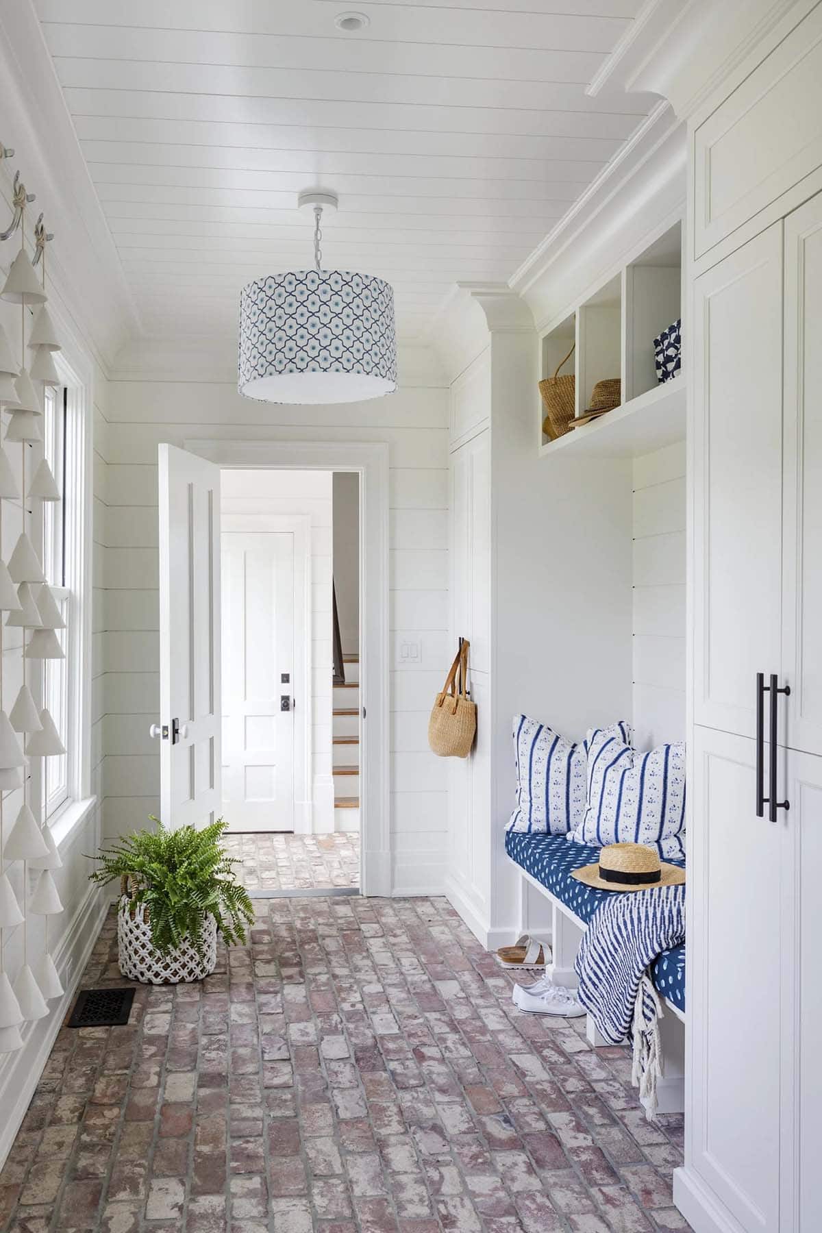 Mudroom hallway with brick flooring and navy striped bench