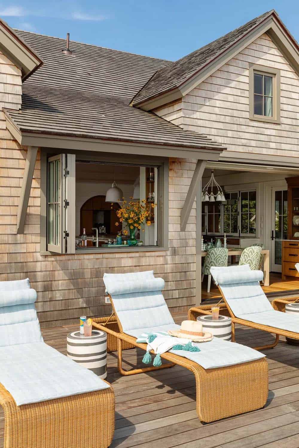 Wicker chaise lounges on wood deck beside open Dutch window into kitchen, sunflowers on sill