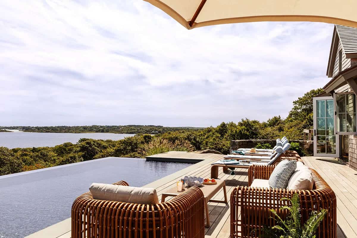 Infinity pool deck overlooking coastal marshland with rattan sofa and umbrella-shaded seating