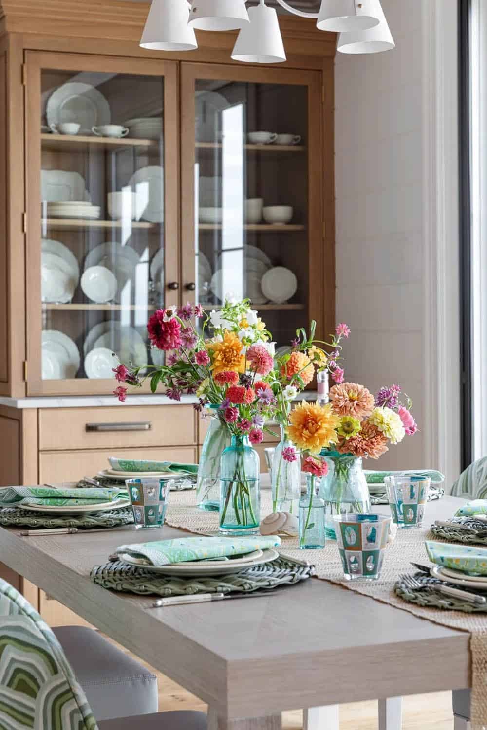 Close-up of dining table set with colorful dahlia bouquets and patterned glassware