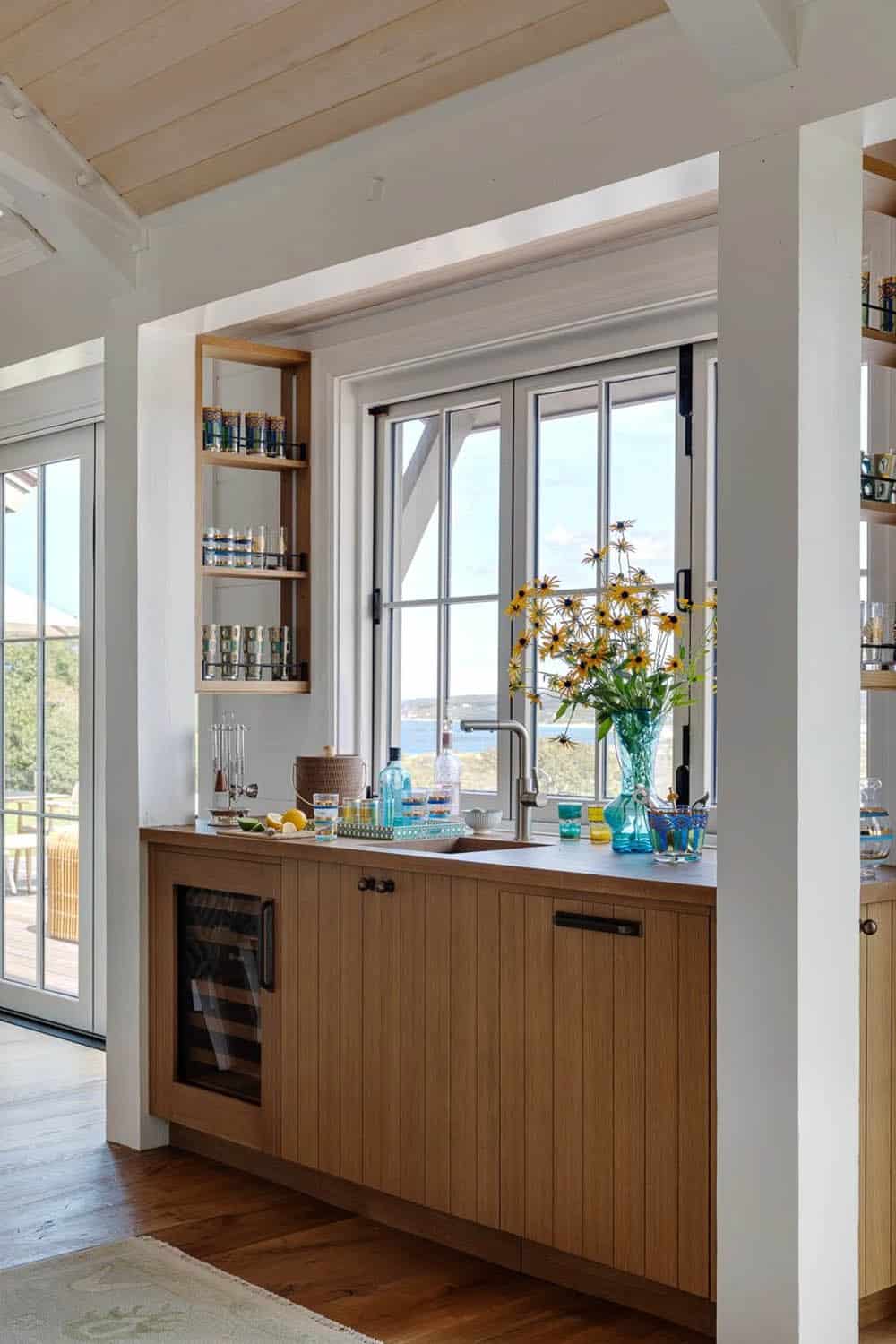 Wood wet bar nook with wall-mounted glass shelves and ocean view through open window