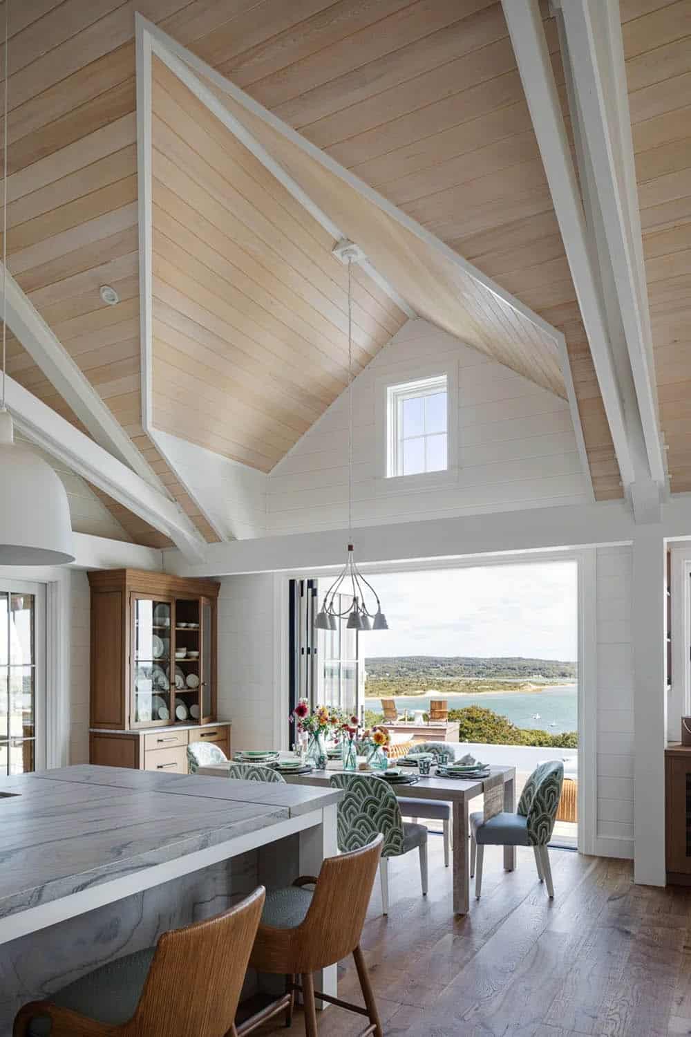Vaulted wood-paneled dining area with folding glass doors opening to ocean view