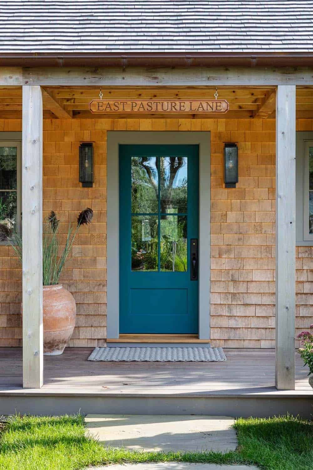 Teal front door under "East Pasture Lane" sign flanked by wall sconces