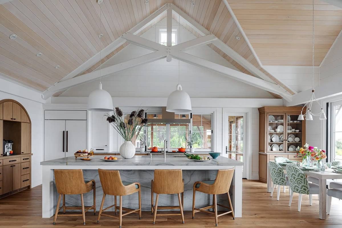 Kitchen island with marble counter, rattan stools, and vaulted timber ceiling