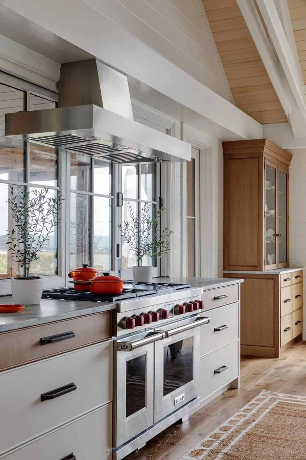 Kitchen range with stainless hood, red Le Creuset pots, and potted olive trees