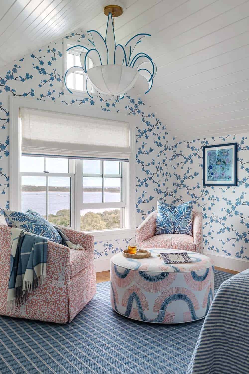 Reading nook with pink patterned armchairs, floral ottoman, and cherry blossom wallpaper by window