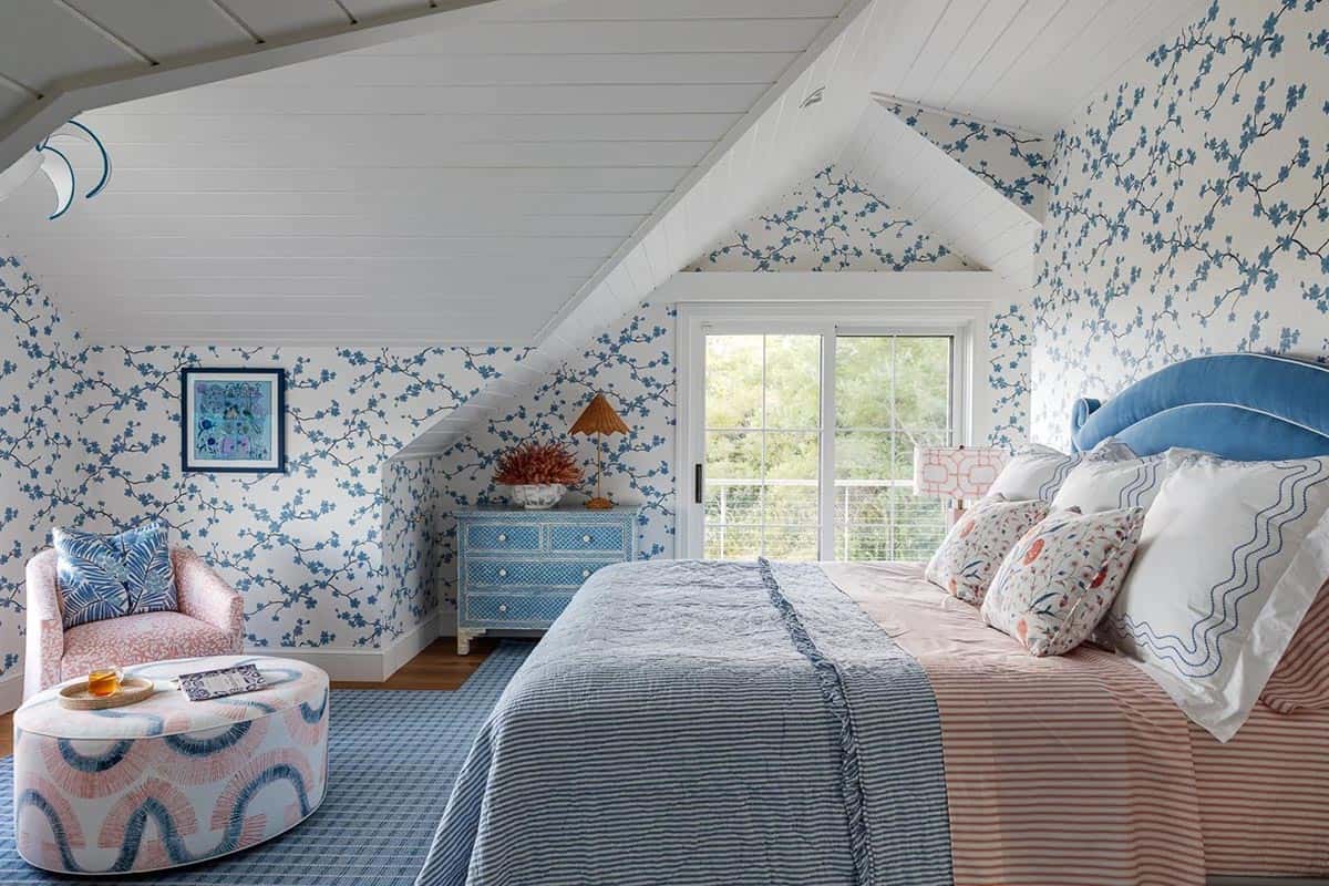 Attic bedroom with sloped ceiling, blue floral wallpaper, blue headboard, and striped bedding