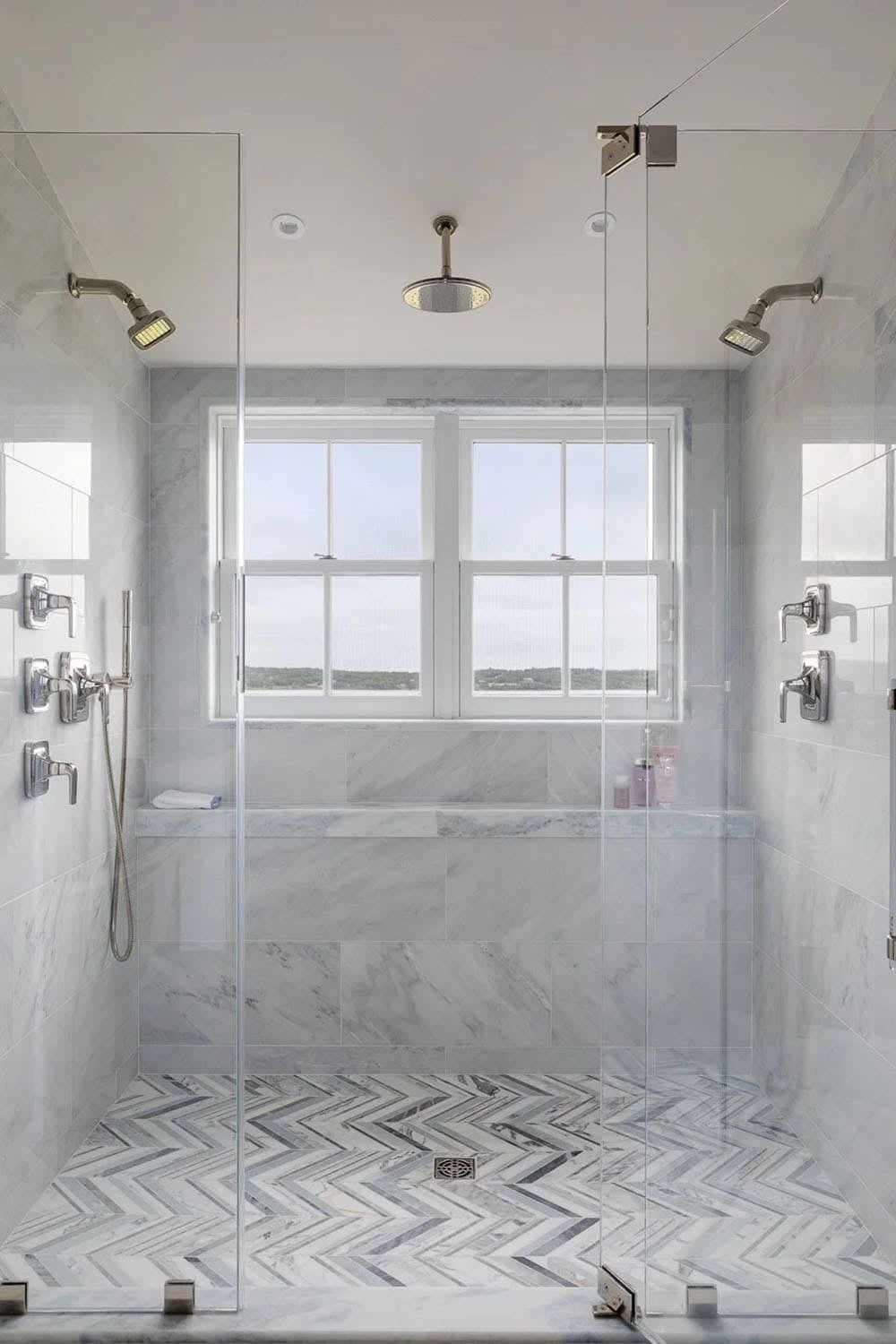 Marble double shower with chevron floor tile and window overlooking landscape