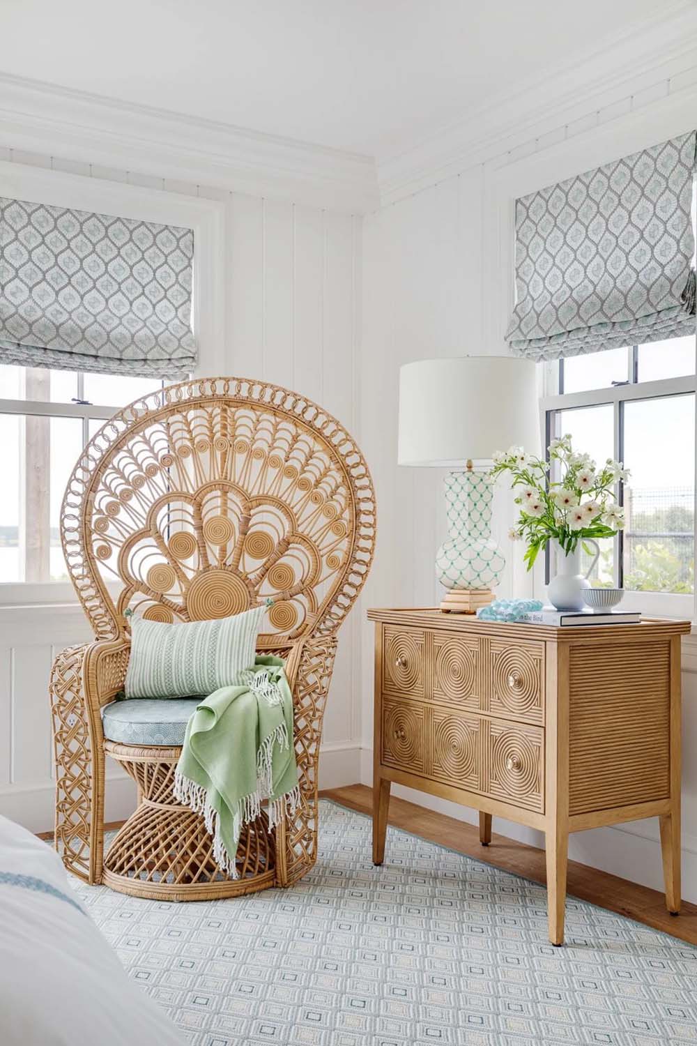Rattan peacock chair beside striped dresser in bedroom with patterned Roman shades