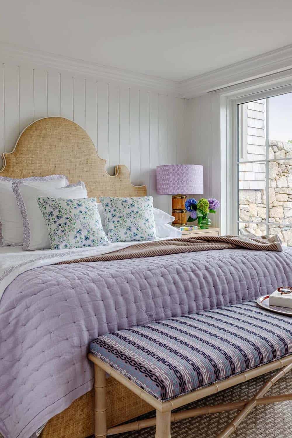 Bedroom with woven headboard, lavender quilt, and striped bamboo bench