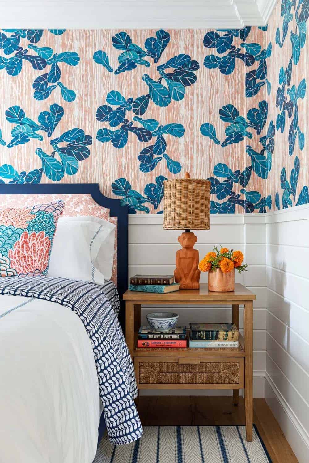 Bedside table with wood monkey lamp against blue leaf and coral-striped wallpaper