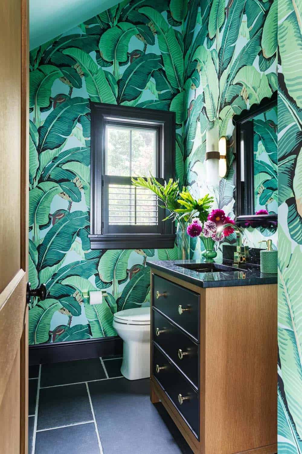 Powder room with green banana-leaf wallpaper, black vanity, and dark tile floor
