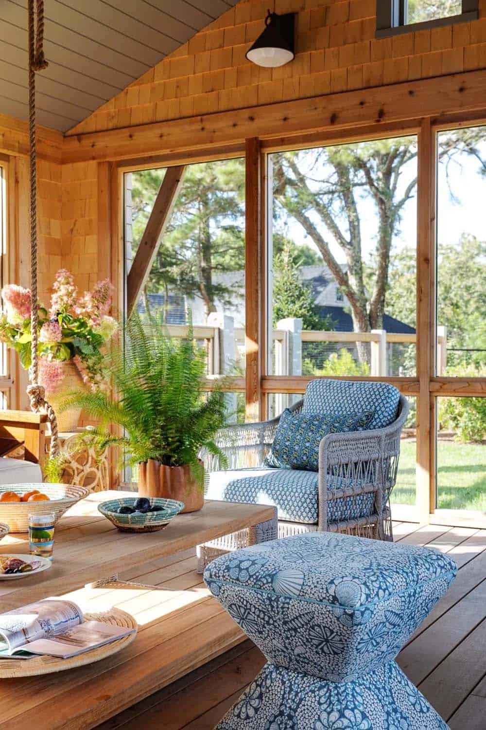 Screened porch corner with woven armchair, patterned ottoman, and wooden table