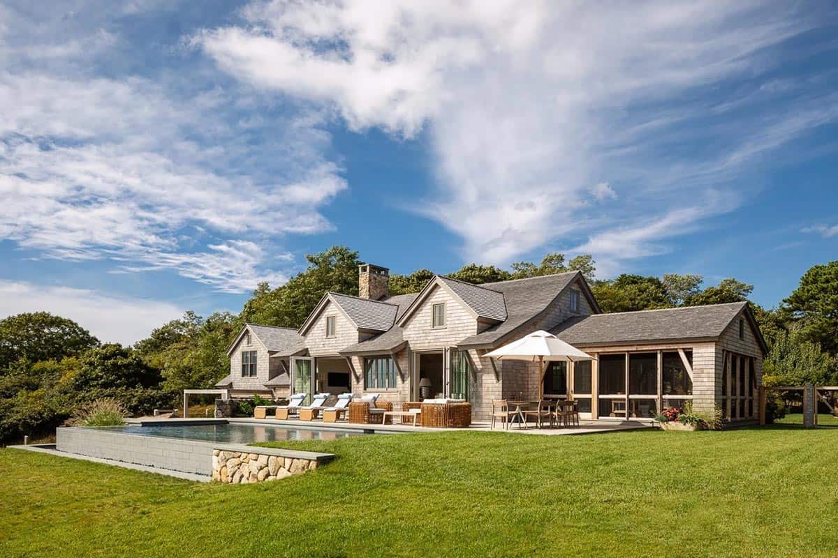 Wide exterior view of shingle-style home with multiple gables, screened porch, and infinity pool on lawn