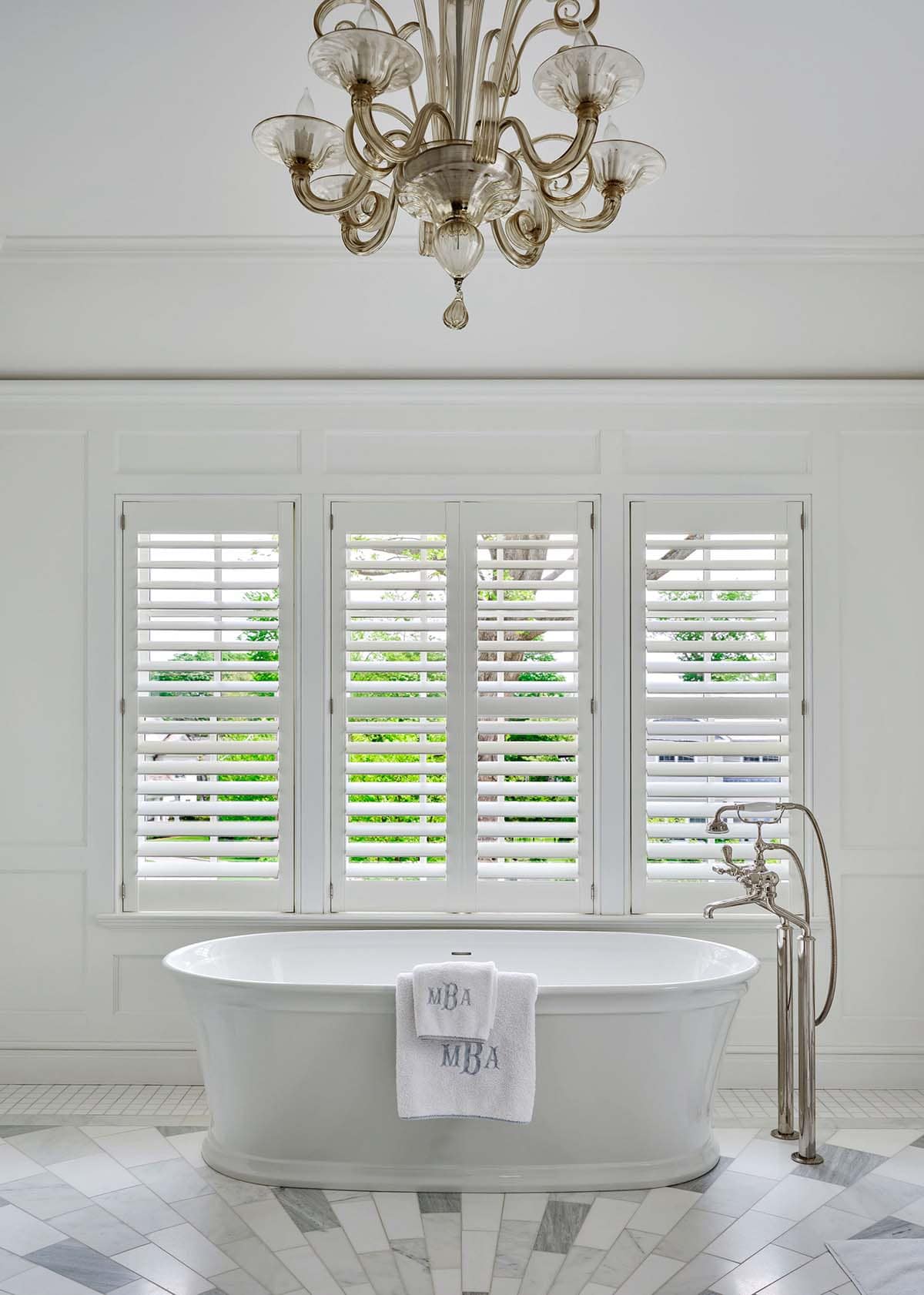 White marble primary bathroom with freestanding tub and glass chandelier