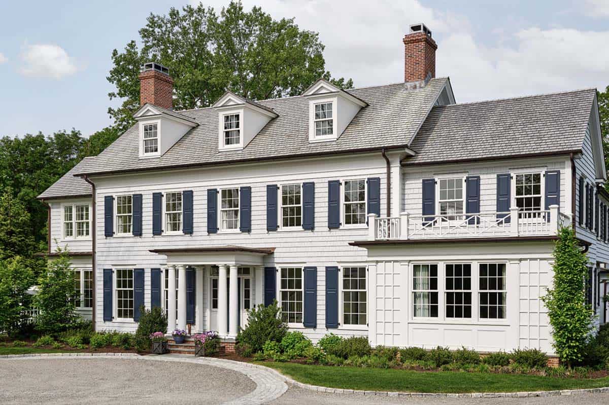 Angled front view of colonial revival home with navy shutters and dormers