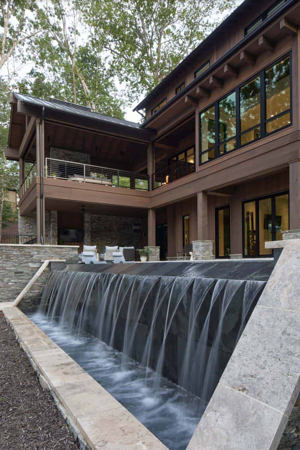 Two-story deck and patio with stone accents beside a spillway waterfall feature