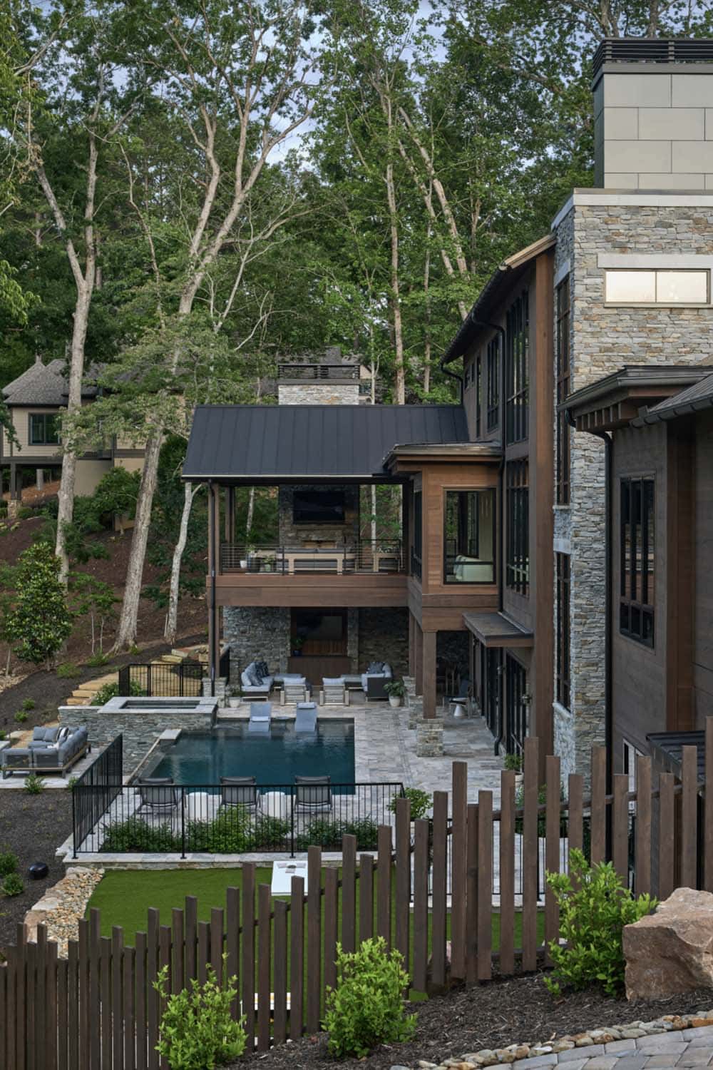 Exterior view of stacked covered porches, stone tower, pool, and spa surrounded by a wood picket fence