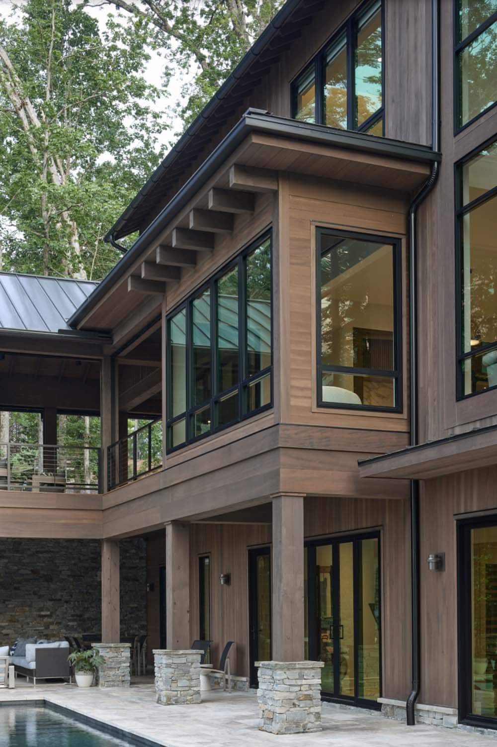 Close-up of exposed timber roof brackets, wood siding, and black-framed windows above the pool patio