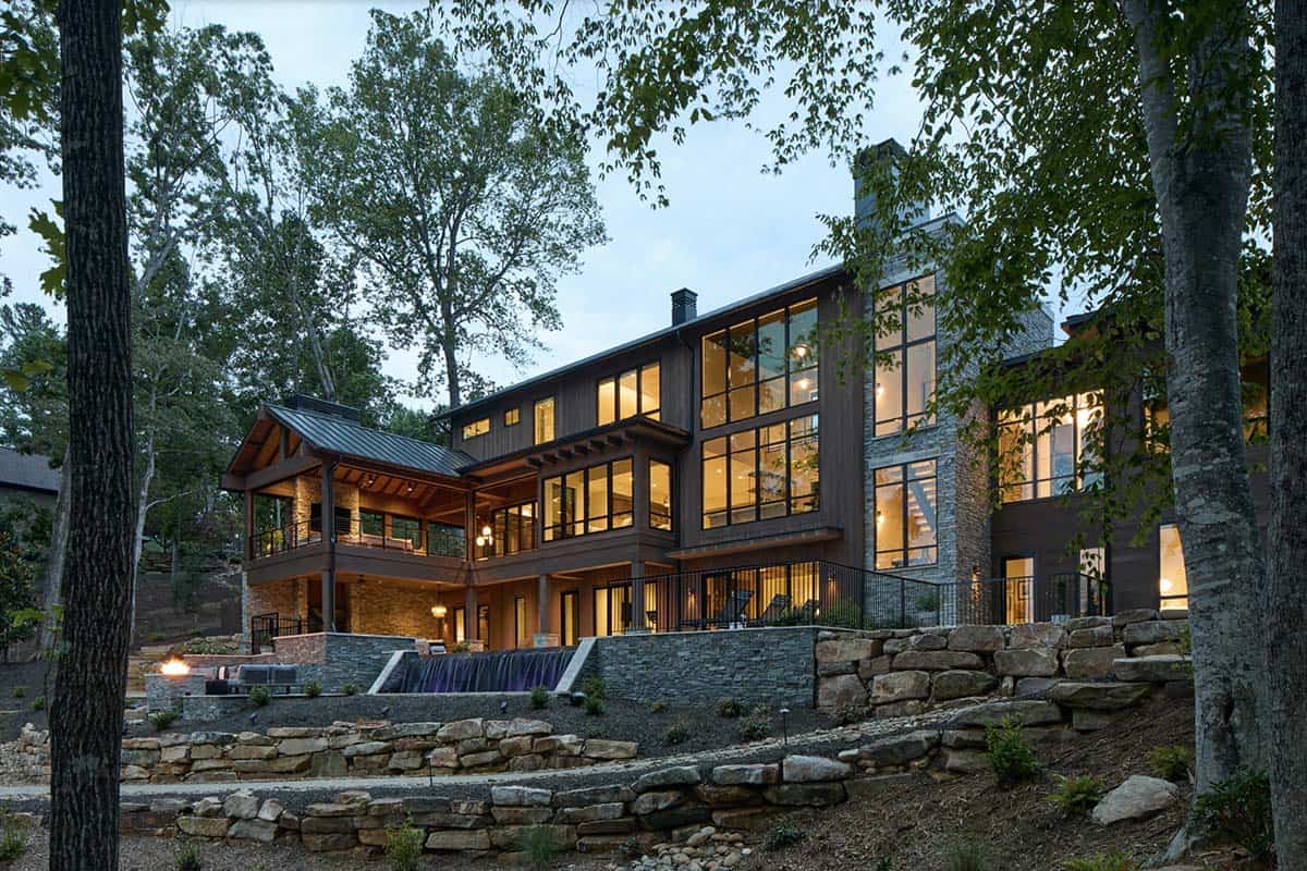 Evening view of the illuminated lake house exterior with stone terracing and a cascading water feature