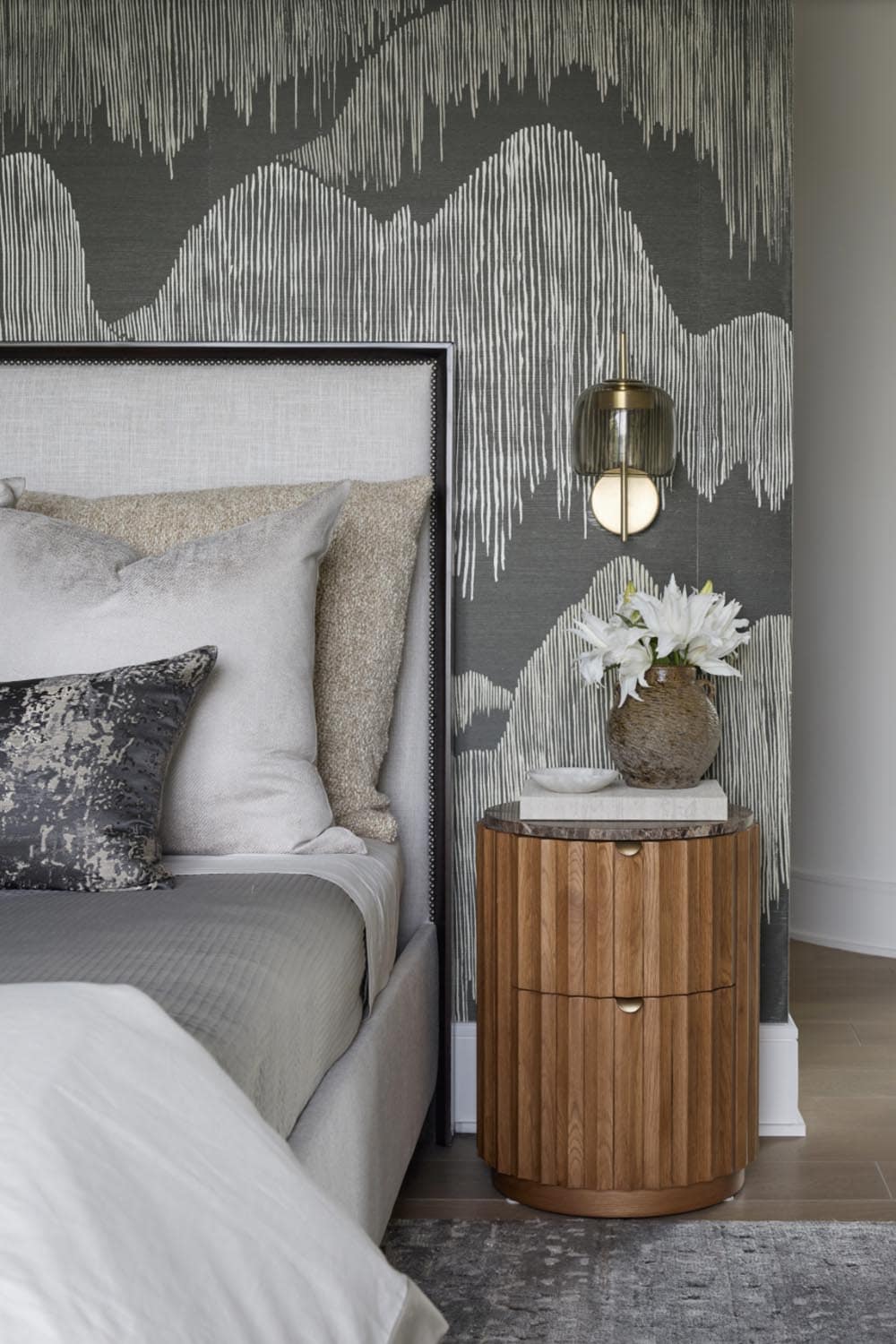 Bedroom nightstand with mountain-pattern wallpaper, brass sconce, and a floral arrangement