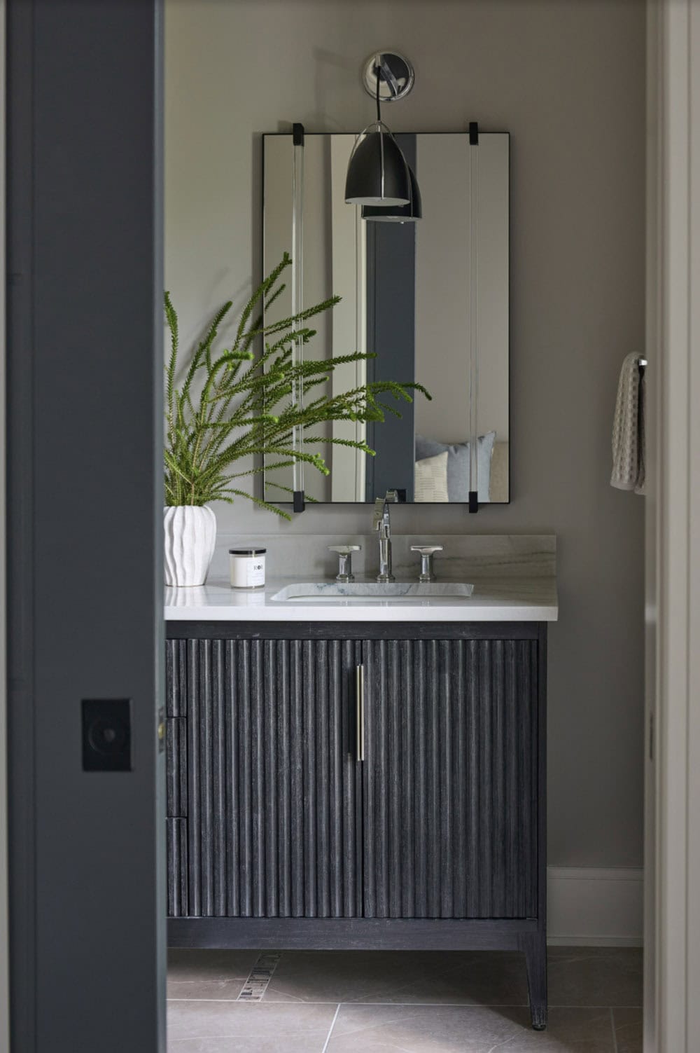 Powder room vanity with fluted dark wood cabinet, marble top, and round mirror with sconce