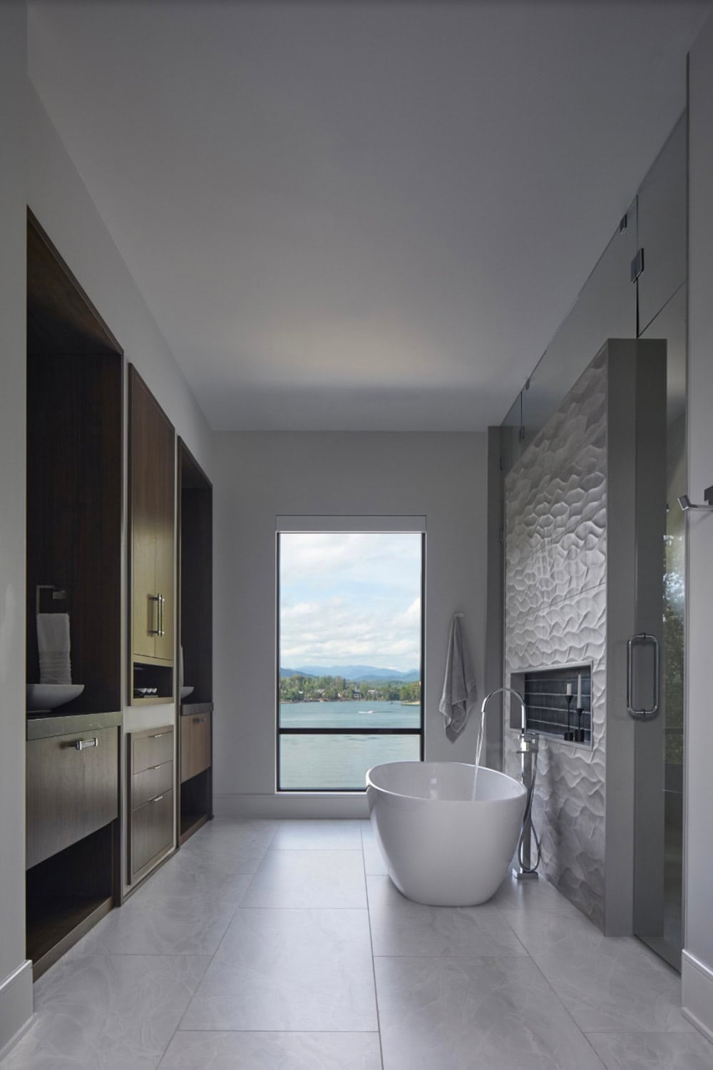 Primary bathroom with freestanding tub, textured tile accent wall, and a lake view window