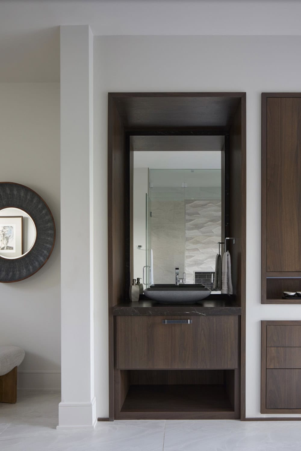 Wood-framed vanity nook with dark stone countertop, vessel sink, and round wall mirror