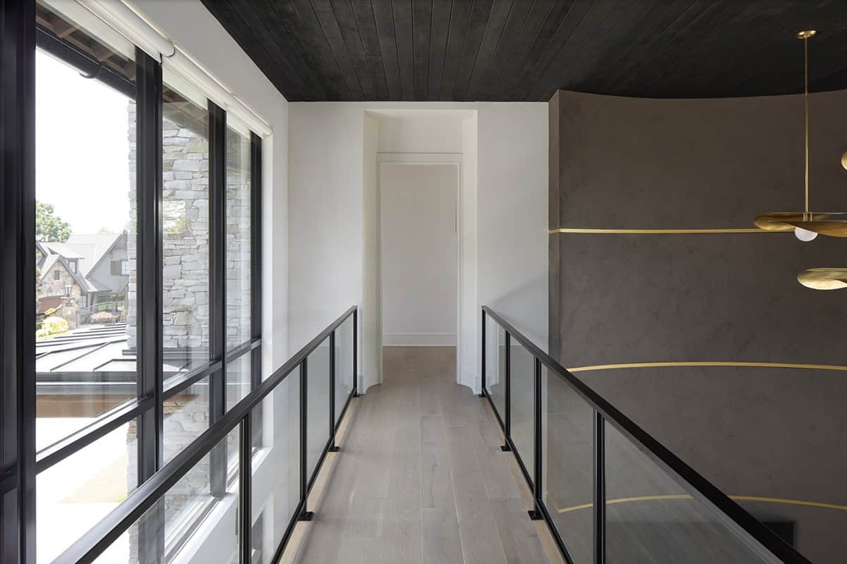 Upper-level hallway with glass railing, dark wood ceiling, and a curved textured accent wall