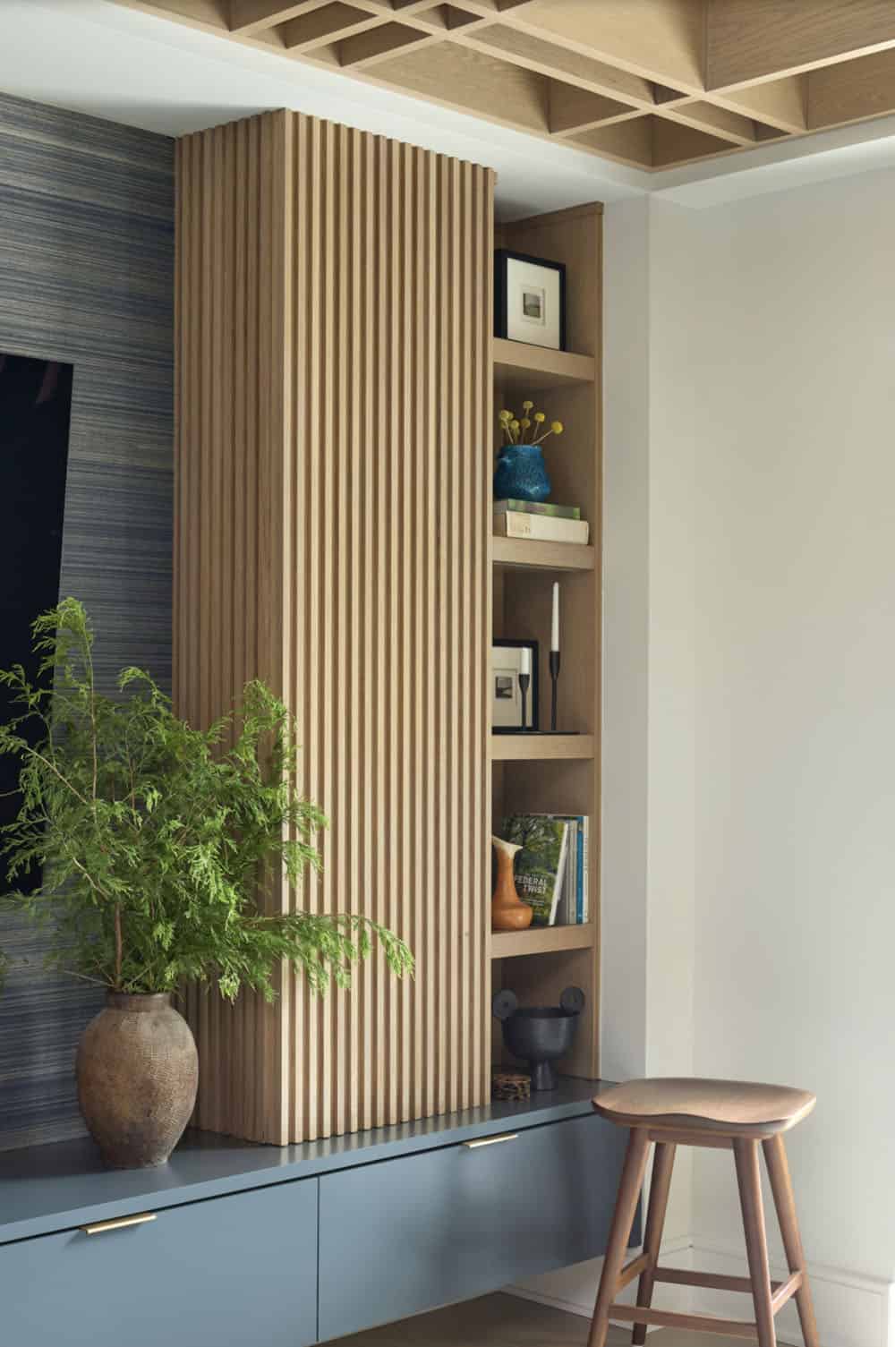 Fluted wood column with built-in display shelving beside a blue credenza and leather stool