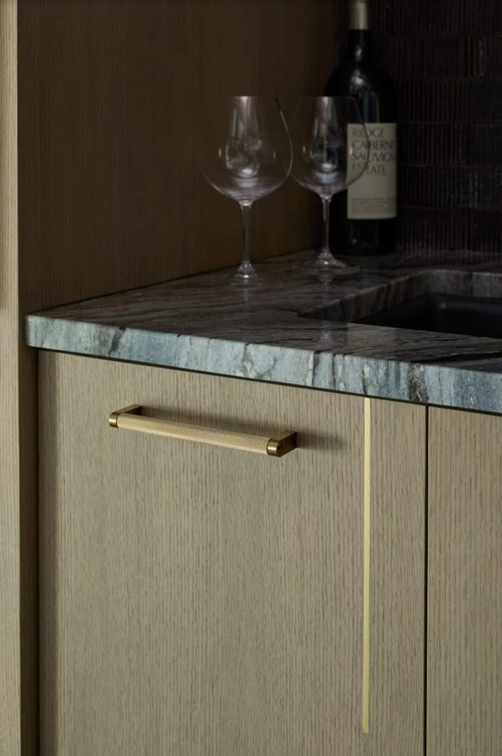 Close-up of a bar cabinet with textured brass pull, marble countertop, and wine glasses