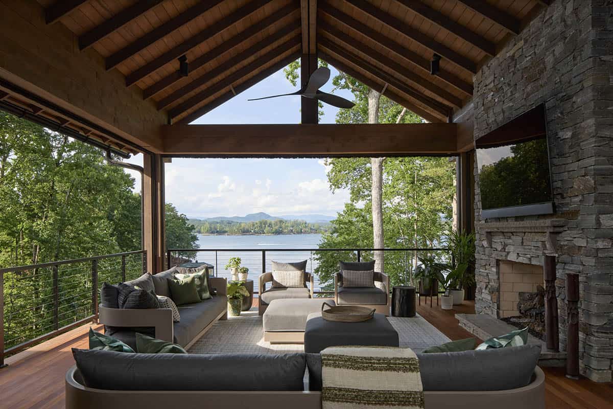 Covered outdoor living room with stone fireplace, sectional seating, and a lake view through open walls