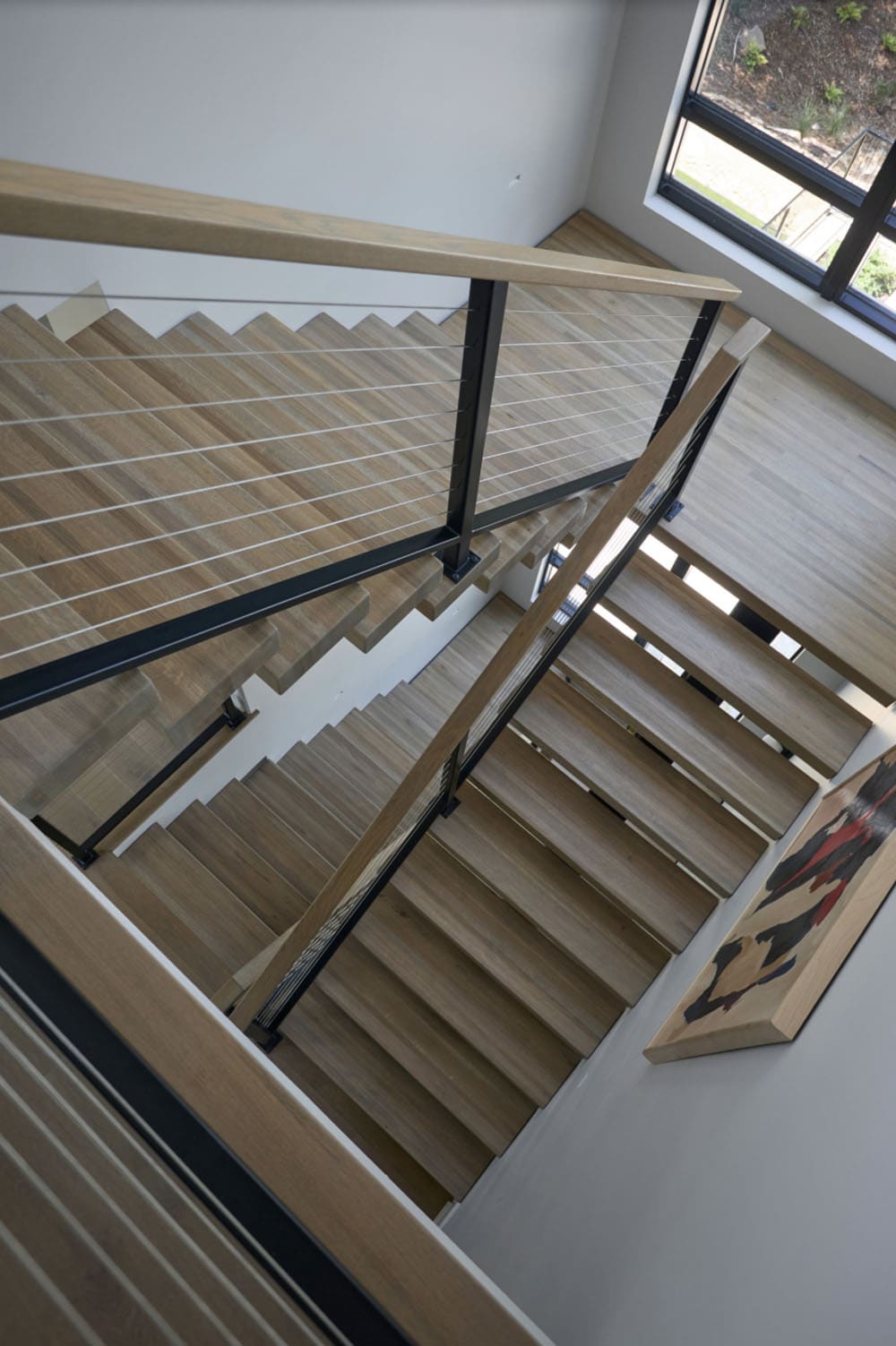 Overhead view down an open-tread staircase with cable railings and wood steps