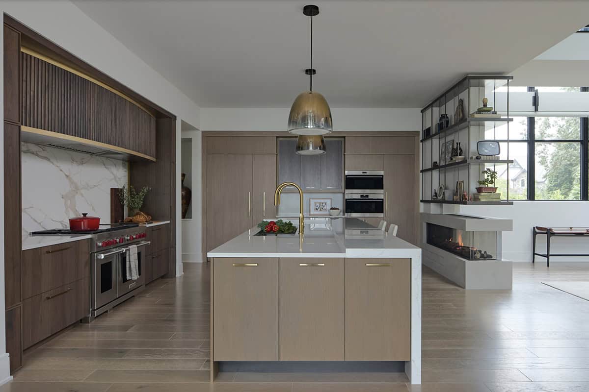 Modern kitchen with marble backsplash, brass fixtures, waterfall island, and a three-sided fireplace