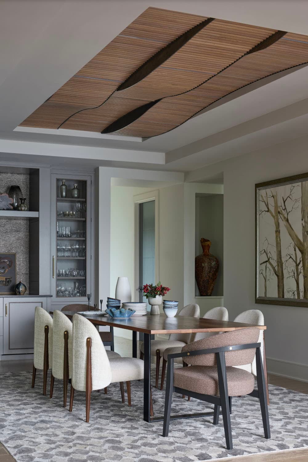 Dining room with a sculptural wavy wood ceiling feature above a wood table and upholstered chairs