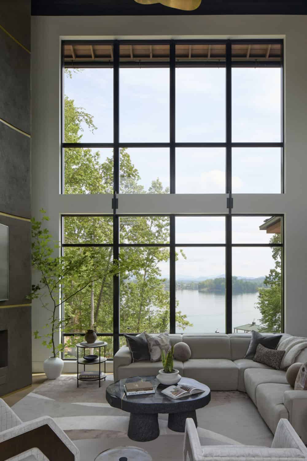 Floor-to-ceiling black-framed windows overlooking the lake in a living room with a sectional sofa